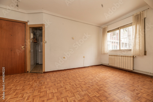 empty room with wooden floors similar to sintasol  aluminum window with bars and white curtains and white aluminum radiators and ceiling with plaster moldings