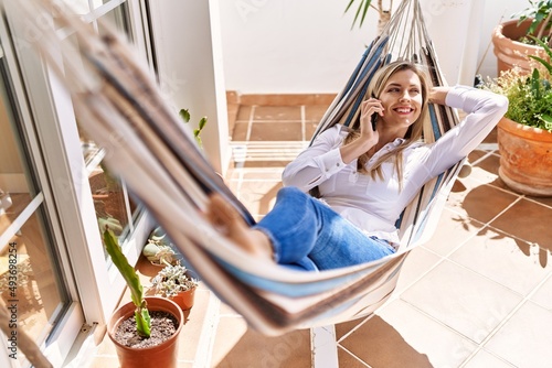 Young blonde woman talking on the smartphone lying on hammock at terrace. photo