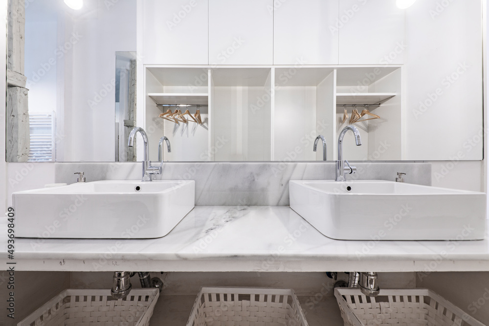 Fototapeta premium Bathroom decorated with twin porcelain sinks on white marble countertops and white painted wicker baskets