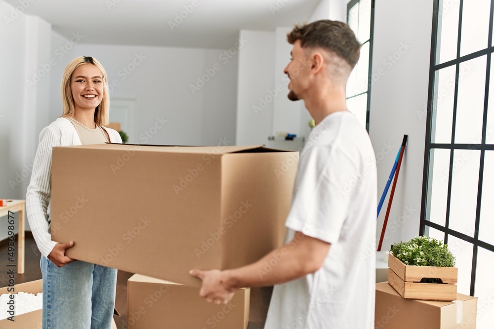 Young caucasian couple smiling happy holding cardboard boxes standing at new home. Young caucasian couple smiling happy holding cardboard boxes standing at new home.