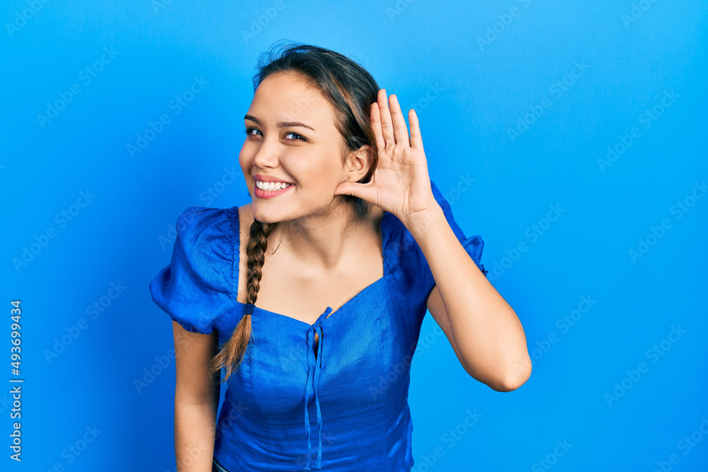 Young hispanic girl wearing casual clothes smiling with hand over ear listening an hearing to rumor or gossip. deafness concept. Young hispanic girl wearing casual clothes smiling with hand over ear listening an hearing to rumor or gossip. deafness concept.