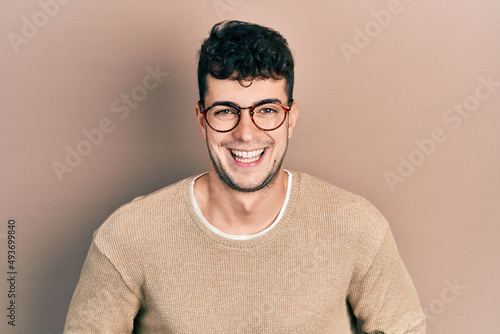 Young hispanic man wearing casual clothes and glasses smiling and laughing hard out loud because funny crazy joke with hands on body.