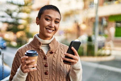 Young hispanic woman with short hair smiling happy drinking a cup of coffee and using smartphone