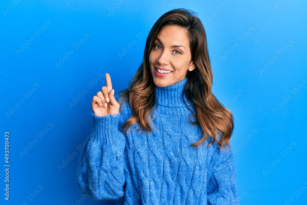 Young latin woman wearing casual winter sweater smiling with an idea or question pointing finger up with happy face, number one Young latin woman wearing casual winter sweater smiling with an idea or question pointing finger up with happy face, number one