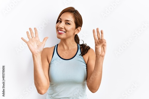 Young latin woman wearing sporty clothes over isolated background showing and pointing up with fingers number eight while smiling confident and happy.