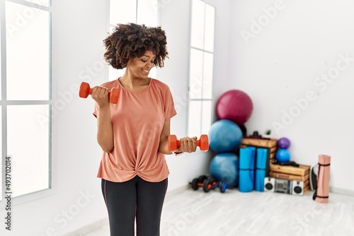 Young african american woman smiling confident training using dumbbells at sport center