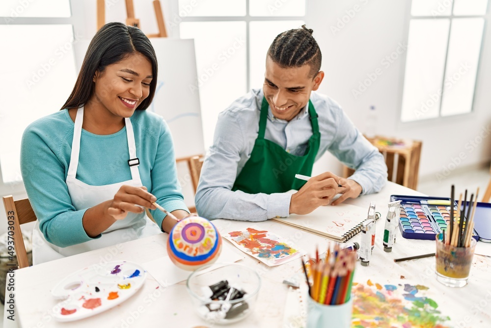 Fototapeta premium Young latin painter couple smiling happy painting sitting on the table at art studio