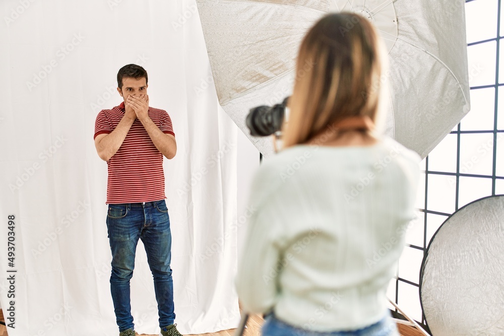 Woman photographer talking pictures of man posing as model at photography studio shocked covering mouth with hands for mistake. secret concept. Woman photographer talking pictures of man posing as model at photography studio shocked covering mouth with hands for mistake. secret concept.