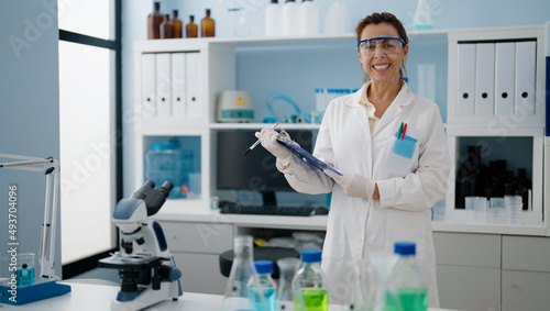 Middle age hispanic woman wearing scientist uniform holding checklist at laboratory