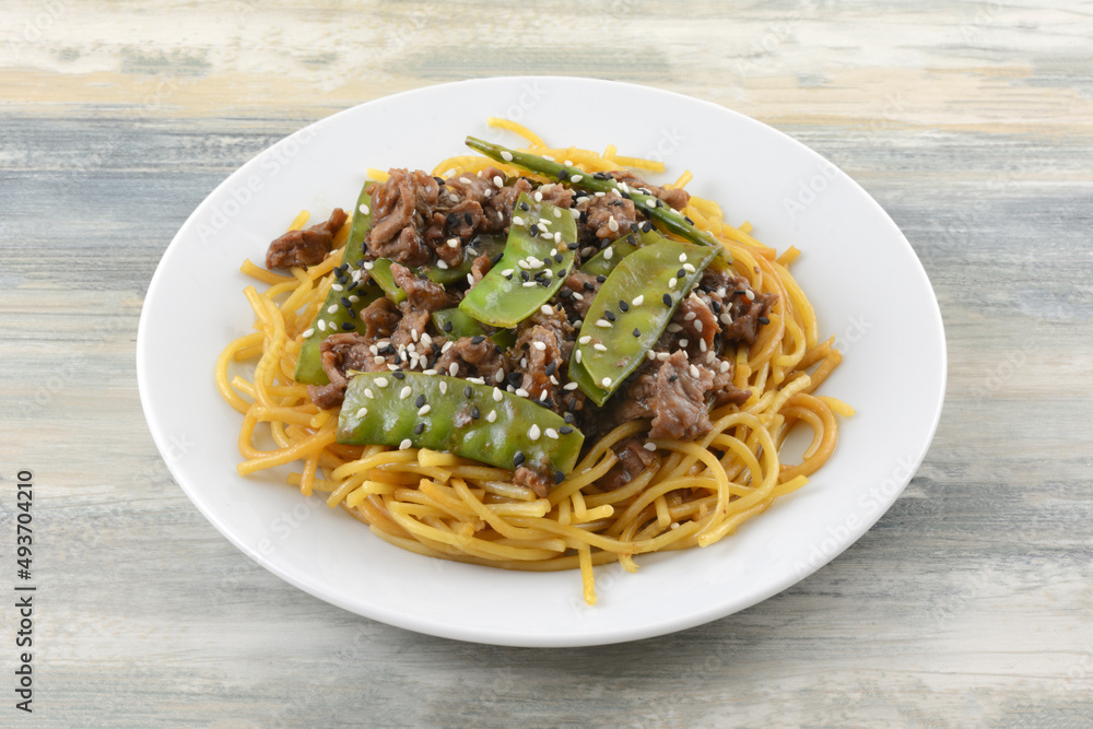 Mongolian style beef with snow peas and sesame seeds on noodles on white late