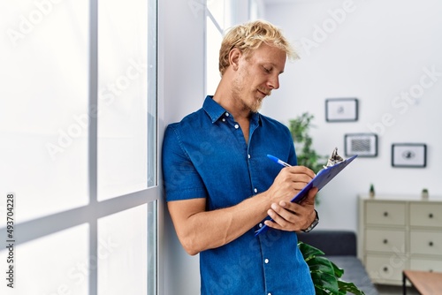 Young caucasian man smiling confident writing on clipboard at home