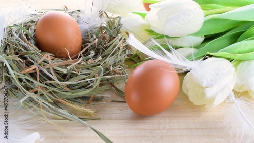 Easter eggs color in basket with spring tulips, white feathers on wooden table background in Happy Easter decoration. Festive decoration