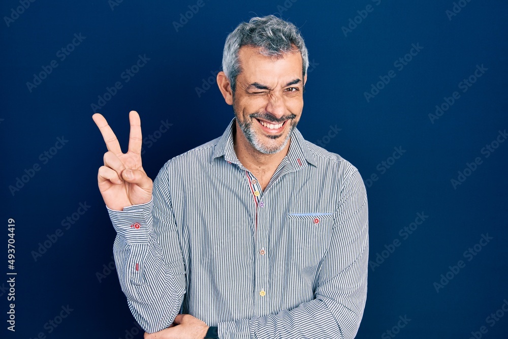 Handsome middle age man with grey hair wearing business shirt smiling with happy face winking at the camera doing victory sign. number two. Handsome middle age man with grey hair wearing business shirt smiling with happy face winking at the camera doing victory sign. number two.