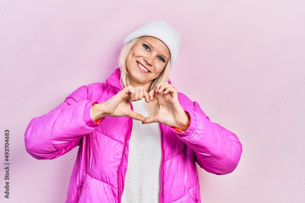 Beautiful caucasian blonde woman wearing wool hat and winter coat smiling in love doing heart symbol shape with hands. romantic concept. Beautiful caucasian blonde woman wearing wool hat and winter coat smiling in love doing heart symbol shape with hands. romantic concept.