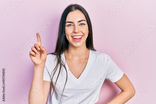 Beautiful woman with blue eyes wearing casual white t shirt smiling with an idea or question pointing finger up with happy face, number one © Krakenimages.com