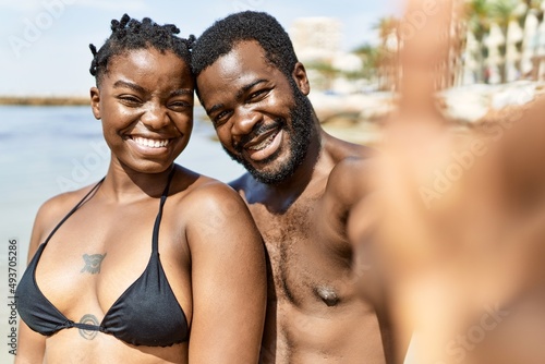 Young african american tourist couple wearing swimwear making selfie by the camera at the beach.