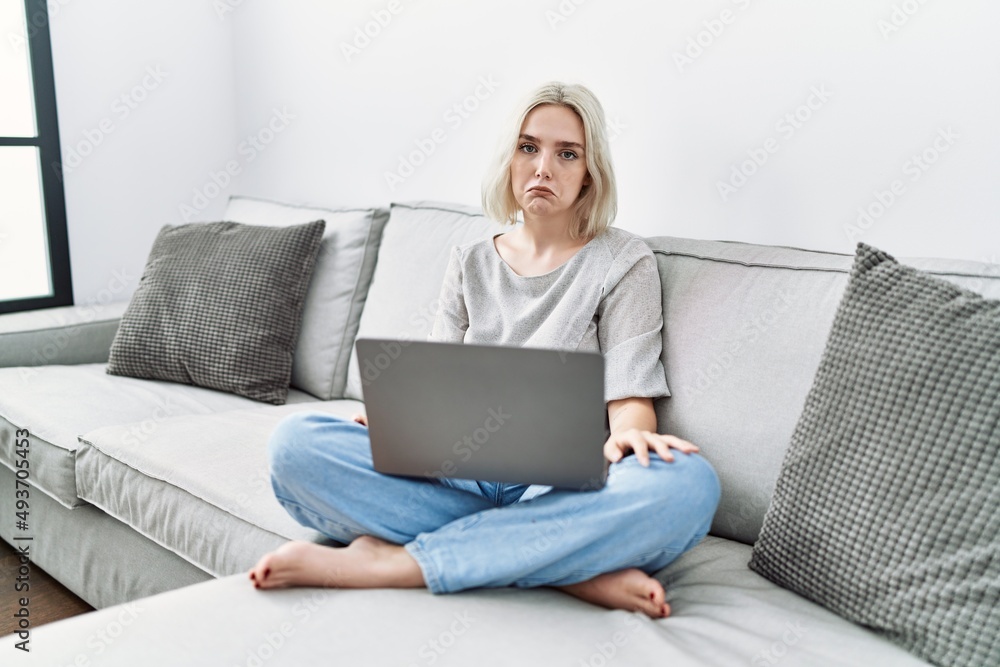 Young caucasian woman using laptop at home sitting on the sofa depressed and worry for distress, crying angry and afraid. sad expression.