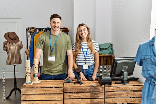 Two hispanic shopkeepers smiling happy standing at clothing store.