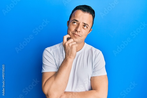 Handsome young man wearing casual white t shirt thinking concentrated about doubt with finger on chin and looking up wondering