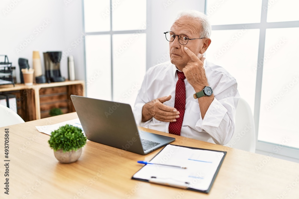 Senior man working at the office using computer laptop pointing to the eye watching you gesture, suspicious expression Senior man working at the office using computer laptop pointing to the eye watching you gesture, suspicious expression