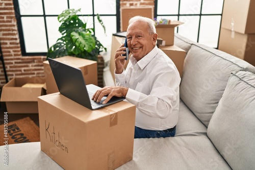 Senior man using laptop talking on the smartphone at new home © Krakenimages.com
