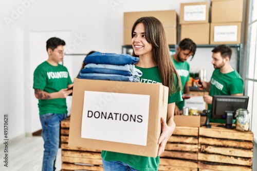 Group of young volunteers working at charity center. Woman smiling happy and holding box with clothes to donate. © Krakenimages.com