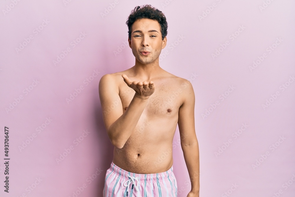 Fototapeta premium Young handsome man wearing swimwear shirtless looking at the camera blowing a kiss with hand on air being lovely and sexy. love expression.