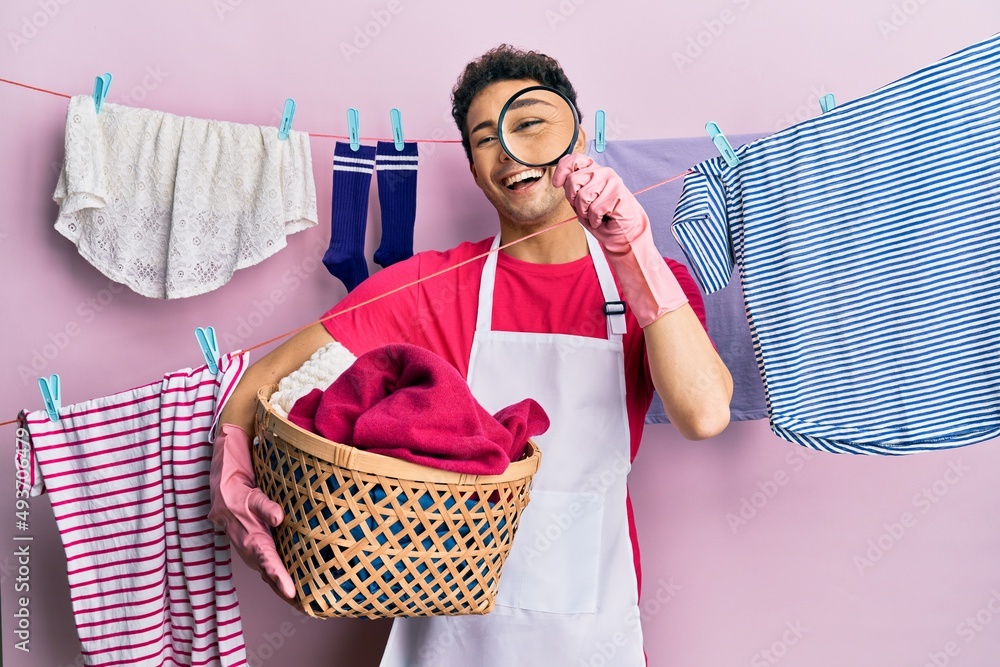 Handsome hispanic man doing laundry holding wicker basket looking for a stain smiling and laughing hard out loud because funny crazy joke. Handsome hispanic man doing laundry holding wicker basket looking for a stain smiling and laughing hard out loud because funny crazy joke.