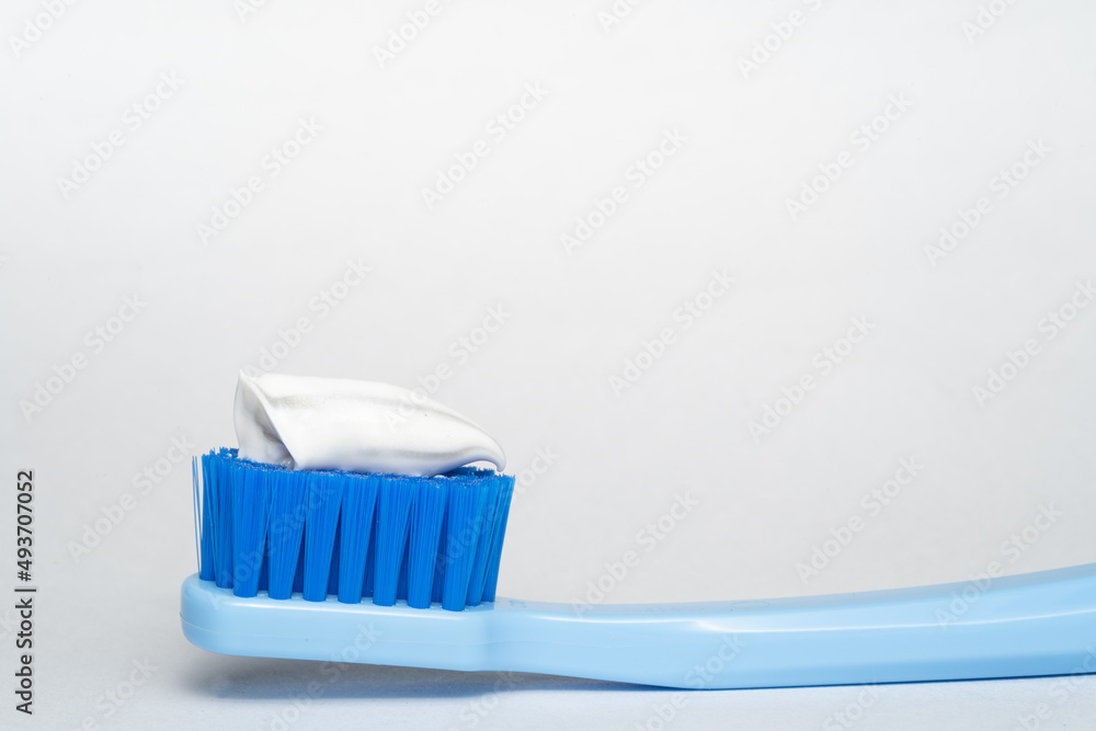 part of blue toothbrush with white toothpaste on a blue white background . Toothbrush closeup on white background. part of blue toothbrush with white toothpaste on a blue white background . Toothbrush closeup on white background.