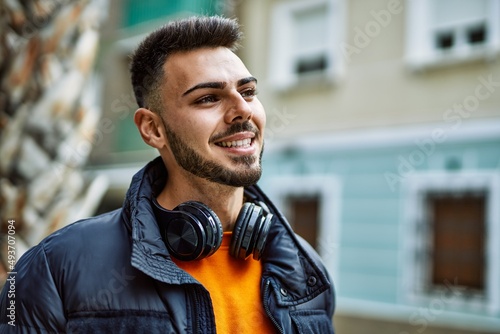 Handsome hispanic man with beard smiling happy and confident at the city wearing winter coat and headphones