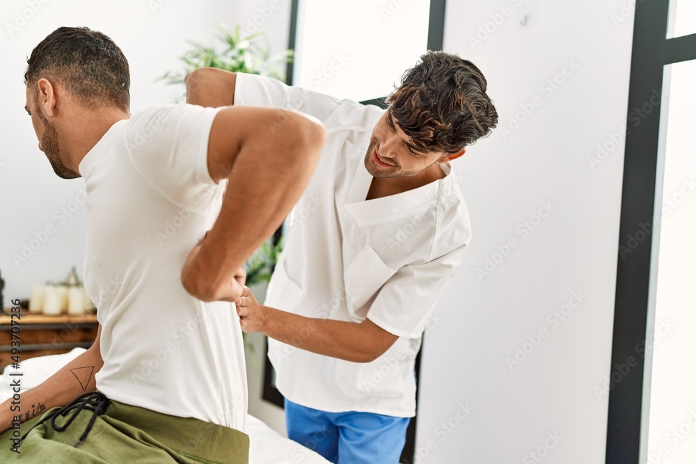 Fototapeta premium Two hispanic men physiotherapist and patient having rehab session massaging back at clinic