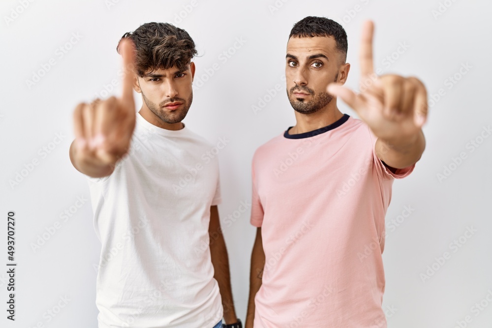 Young gay couple standing over isolated background pointing with finger up and angry expression, showing no gesture Young gay couple standing over isolated background pointing with finger up and angry expression, showing no gesture