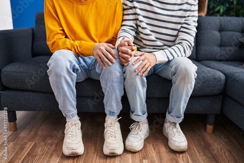 Two man couple sitting on sofa with hands together at home
