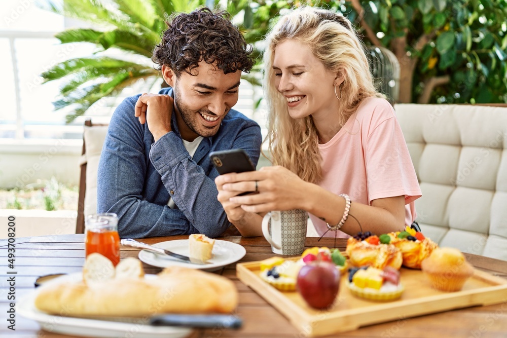Young couple having breakfast and using smartphone sitting on the table at terrace.