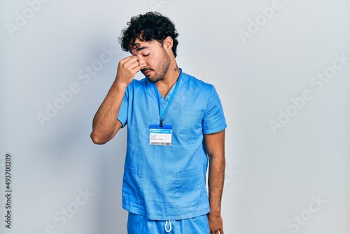 Canvastavla Young hispanic man wearing blue male nurse uniform tired rubbing nose and eyes feeling fatigue and headache