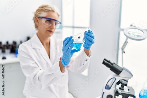 Middle age blonde woman wearing scientist uniform holding test tube at laboratory