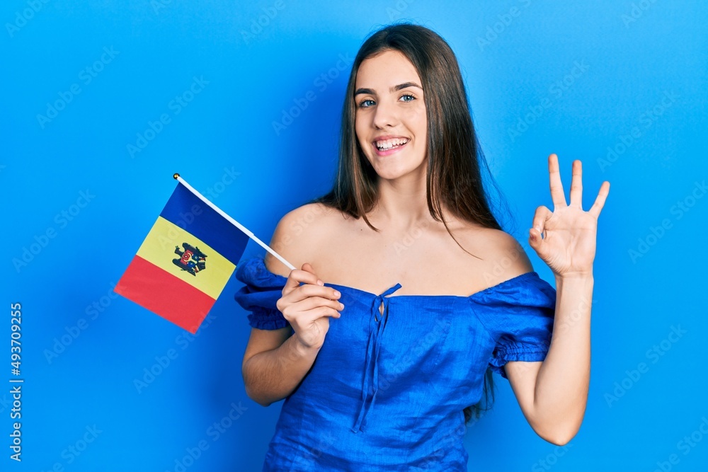 Young brunette teenager holding moldova flag doing ok sign with fingers, smiling friendly gesturing excellent symbol