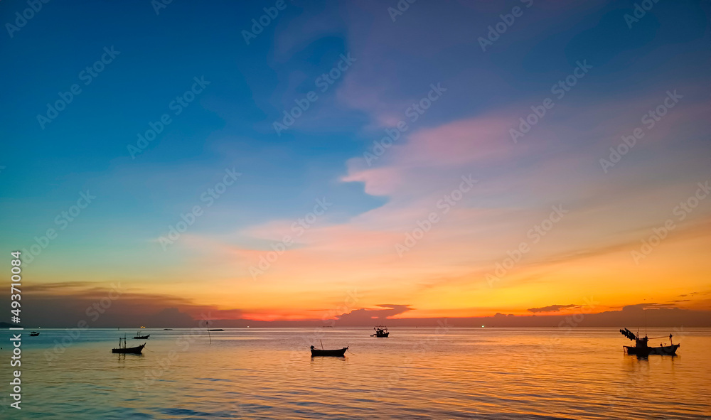Fototapeta premium Sky and sea at sunset, local boats floating in the middle of the sea, orange and blue sky reflecting the sea, giving a calm feeling.
