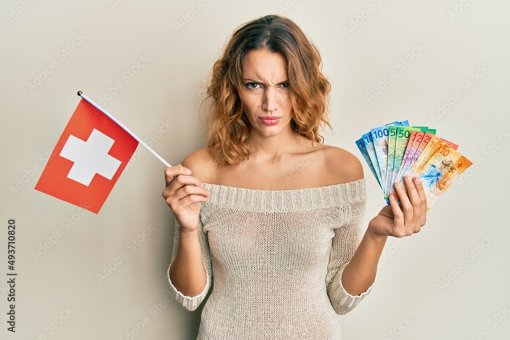 Young caucasian woman holding switzerland flag and franc banknotes skeptic and nervous, frowning upset because of problem. negative person.