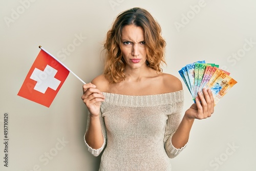 Fototapeta Young caucasian woman holding switzerland flag and franc banknotes skeptic and nervous, frowning upset because of problem