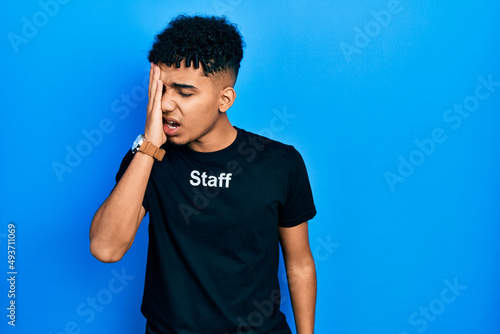 Young african american man wearing staff t shirt yawning tired covering half face, eye and mouth with hand. face hurts in pain.