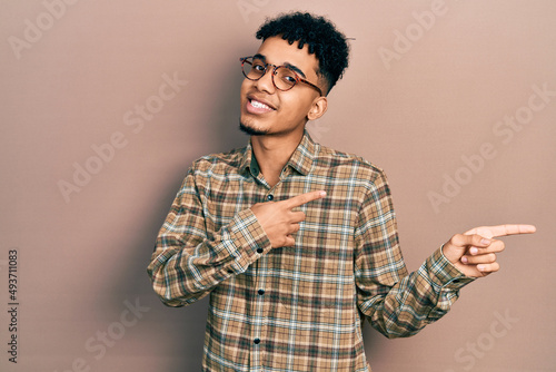 Young african american man wearing casual clothes and glasses smiling and looking at the camera pointing with two hands and fingers to the side.