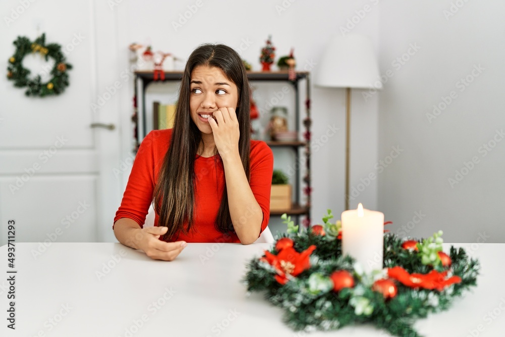 Young brunette woman sitting on the table on christmas looking stressed and nervous with hands on mouth biting nails. anxiety problem. Young brunette woman sitting on the table on christmas looking stressed and nervous with hands on mouth biting nails. anxiety problem.