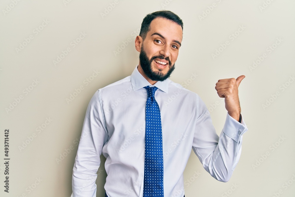 Young man with beard wearing business tie smiling with happy face looking and pointing to the side with thumb up. Young man with beard wearing business tie smiling with happy face looking and pointing to the side with thumb up.