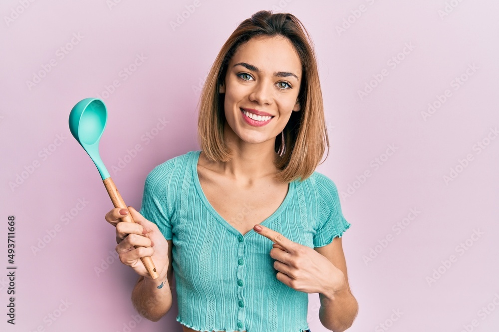 Young caucasian blonde woman holding silicone soup spoon smiling happy pointing with hand and finger Young caucasian blonde woman holding silicone soup spoon smiling happy pointing with hand and finger