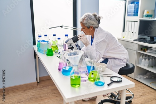 Middle age woman wearing scientist uniform using microscope at laboratory