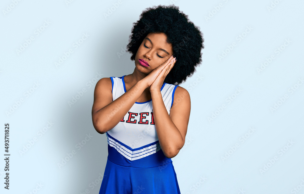 Young african american woman wearing cheerleader uniform sleeping tired dreaming and posing with hands together while smiling with closed eyes. Young african american woman wearing cheerleader uniform sleeping tired dreaming and posing with hands together while smiling with closed eyes.
