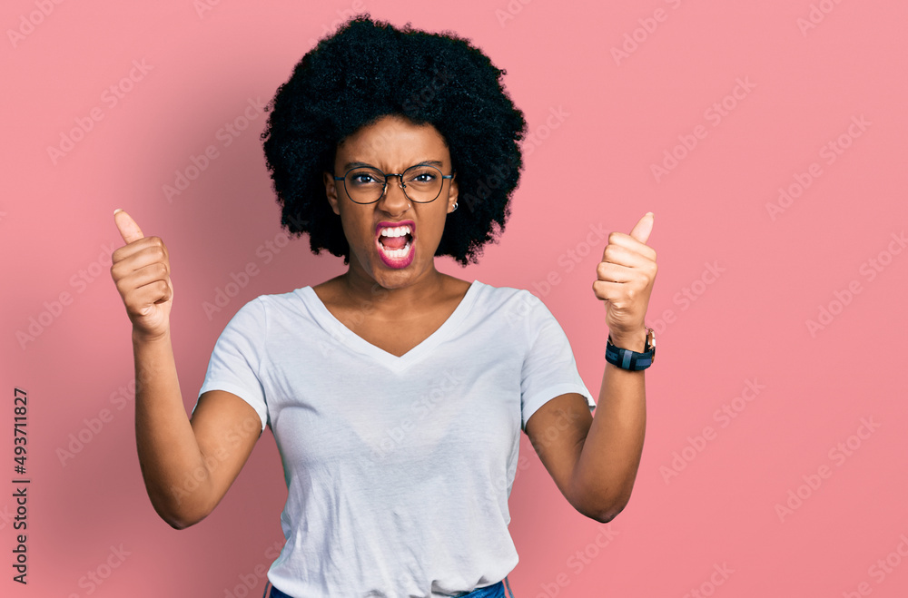 Young african american woman wearing casual white t shirt angry and mad raising fists frustrated and furious while shouting with anger. rage and aggressive concept. Young african american woman wearing casual white t shirt angry and mad raising fists frustrated and furious while shouting with anger. rage and aggressive concept.