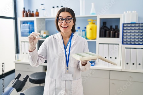 Young hispanic woman working at scientist laboratory with blood samples celebrating crazy and amazed for success with open eyes screaming excited.