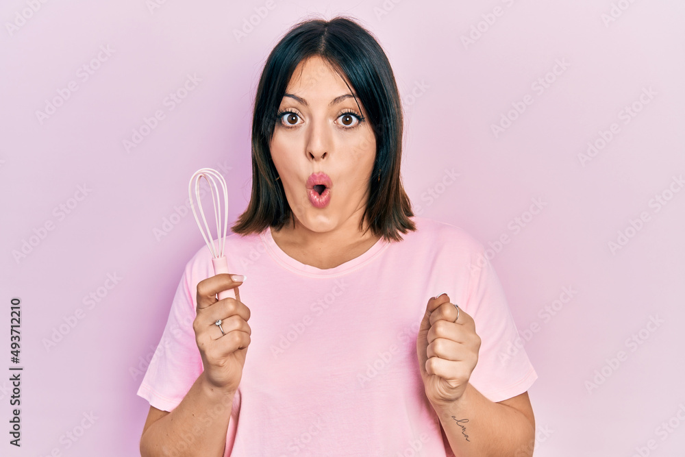 Young hispanic woman cooking using baker whisk scared and amazed with open mouth for surprise, disbelief face Young hispanic woman cooking using baker whisk scared and amazed with open mouth for surprise, disbelief face